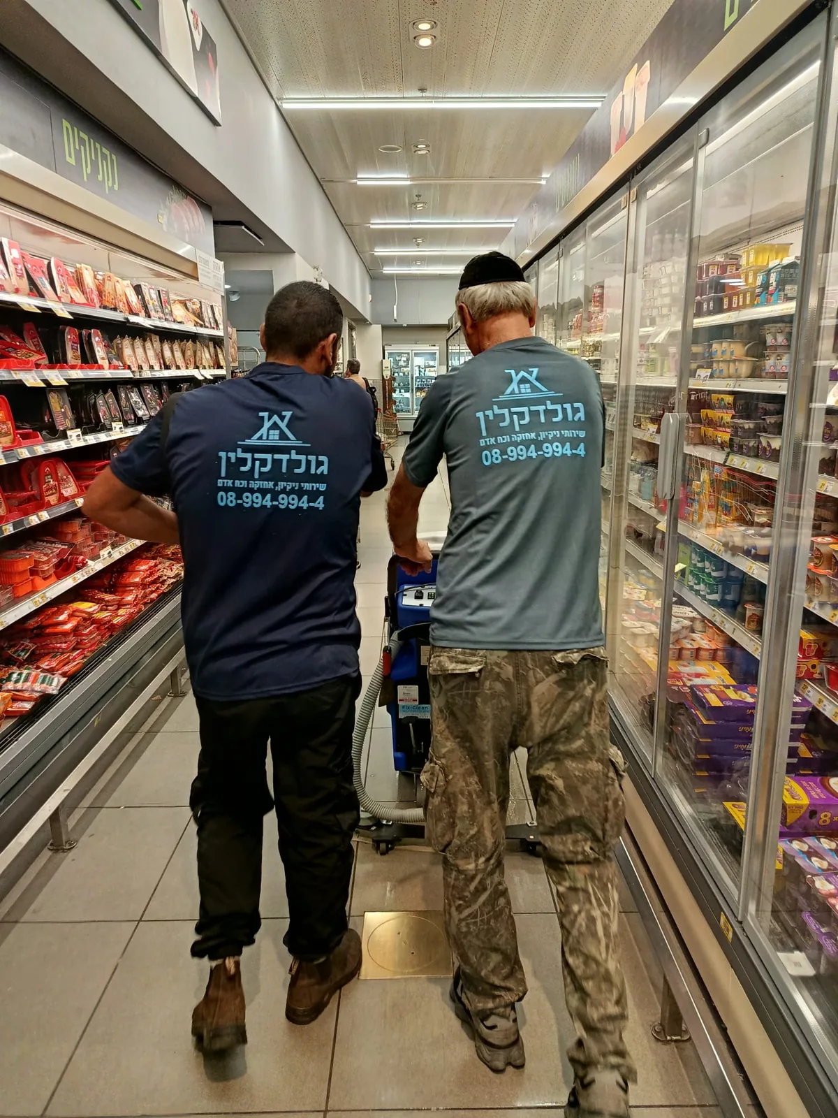 צוות גולד קלין בחולצות החברה מנקה מעבר בסופרמרקט עם מכונת שטיפה
